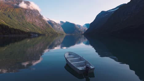 Beautiful-scenery-of-a-small-wooden-row-boat-laying-in-a-large-lake-on-a-sunny-day,-surrounded-by-large-mountains-at-Norway-Lovatnet
