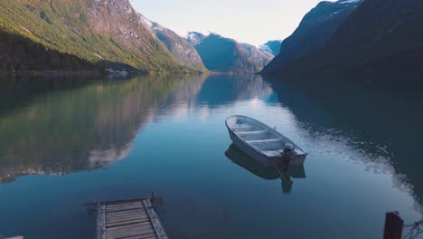 Scenic-view-of-a-small-boat-laying-at-the-dock-of-a-large-lake,-surrounded-by-mountains-in-Norway,-Lovatnet