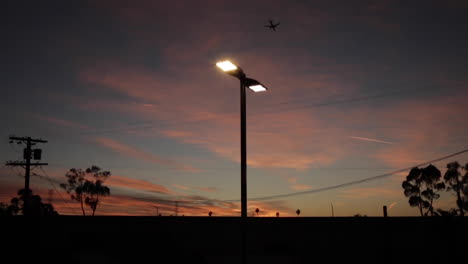 Urban-Sunset,-Plane-Flying-Past-Telephone-Wires-and-Freeway-in-Slow-Motion,-Beautiful