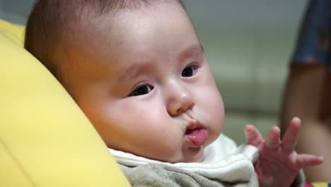 Little-Infan-Three-month-old-baby-lying-on-a-yellow-cushion-and-turning-face-from-side-to-side,-feeble,-close-up,-side-view