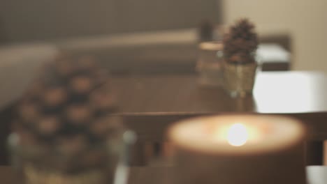 Close-up-of-a-modern-design-wooden-candle-and-a-pinecone-on-a-table-in-a-hotel-lobby-with-a-wooden-table-with-another-candle-and-a-pinecone-in-the-background