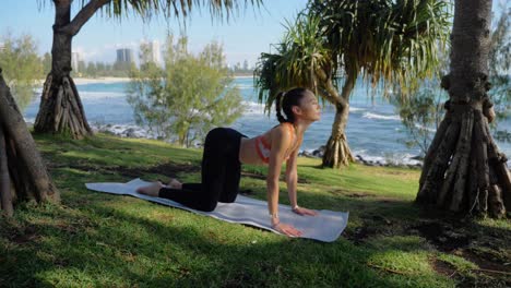Junge-Frau-In-Sportkleidung,-Die-Yoga-Posen-Gegen-Rückenschmerzen-Macht---Katze-zu-Kuh-Yoga-Pose-Übung-Auf-Matte---Burleigh-Heads-Beach-In-Queensland,-Australien