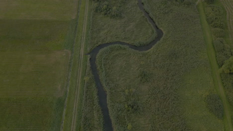Aerial-flight-over-winding-river-through-scenic-flat-grassy-farmland-in-Debki-Poland