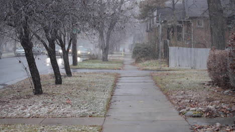 Snow-Falling-on-Sidewalk-of-Residential-Neighborhood-as-Cars-Speed-By-on-Busy-Street