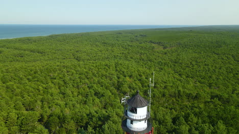 Aerial-drone-shot-down-Stilo-lighthouse-in-Poland-among-thick-green-forest-trees