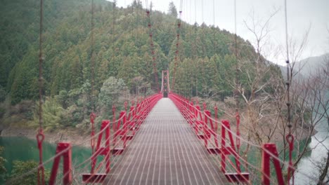 Red-Zaobashi-Suspension-Bridge-Spanning-Across-Arita-River-With-A-Lush-Mountain-Forest-In-The-Background-In-Wakayama,-Japan