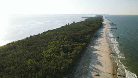 Aerial-side-movement-over-the-forest,-white-sand-beach,-and-baltic-sea-in-Kuznica,-Pomeranian-Voivodeship-,-a-district-of-the-seaside-town-of-Jastarnia
