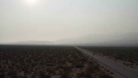Cars-drives-through-the-Mojave-Desert-into-the-haze-caused-by-nearby-wildfires---aerial-view