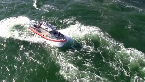 Ariel-view-of-a-US-Coast-Guard-vessel-initially-reversing,-then-moving-forward-along-a-travelled-waterway