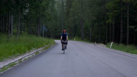Cyclist-with-red-helmet-cycling-through-a-forest-on-early-morning-with-model-release,-Dolomites-Italy