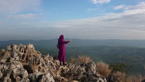Islamic-woman-in-purple-burqa-holding-hands-out-in-prayer-to-god-on-mountain