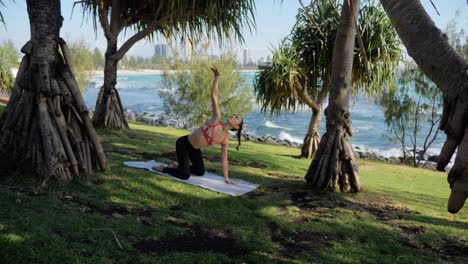 Yogi-On-Yoga-Mat-Exercising-And-Doing-The-Kneeling-Twist-Pose---Lifting-One-Arm-Up-And-Look-Up-Towards-Her-Outstretched-Hand---Burleigh-Heads-Beach-In-Gold-Coast,-QLD,-Australia
