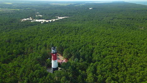 Drone-slow-pull-out-from-Stilo-Lighthouse-and-green-forest-around-it---lighthouse-located-in-Osetnik-on-the-Polish-coast-of-the-Baltic-Sea,-close-to-the-village-of-Sasino,-aerial