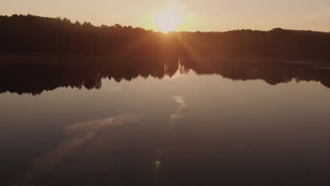 Überfliegen-Des-Ruhigen-Sees-Mit-Einem-Mann,-Der-Während-Eines-Feurigen-Orangefarbenen-Sonnenuntergangs-In-Polen-Ein-Boot-über-Das-Ruhige-Wasser-Paddelt