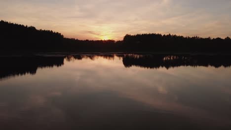 Schöner-Sonnenuntergang-Am-Ruhigen-See,-Umgeben-Von-Bäumen-In-Der-Silhouette-In-Rogowko,-Polen---Niedriger-Luftdrohnenschuss