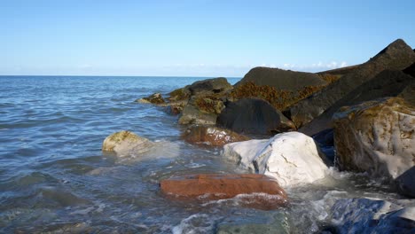 Clear-blue-ocean-tide-washing-onto-colourful-stone-pebble-beach-coastline-island-holiday-scene-dolly-left