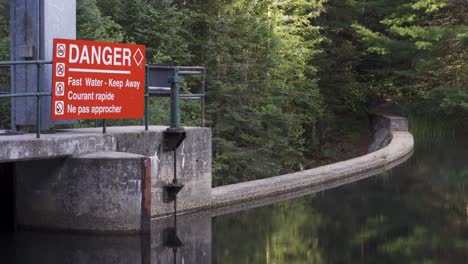 Lake-Spillway-Dam-Infrastruktur-In-Naturlandschaft,-Gefahrenzeichen-Und-Baumreflexionen