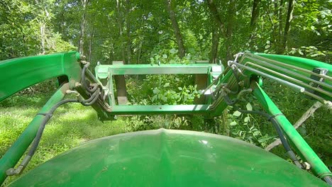 POV-of-equipment-operator-using-a-loader-with-forks-to-push-a-small-pile-of-tree-limbs-in-a-clearing-in-the-woods