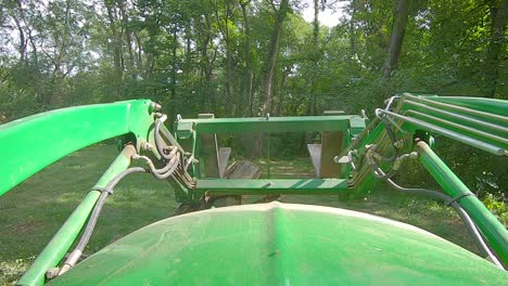 POV-of-equipment-operator-using-a-loader-with-forks-to-move-a-tree-stump-with-roots-and-ivy-in-an-yard-surrounded-by-woods