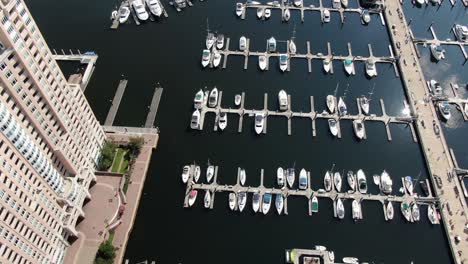 Top-down-aerial-of-boats,-ships,-yachts-docked-at-Baltimore-Inner-Harbor-Marina-in-Maryland,-USA,-waterfront-condo-building,-wealthy,-affluent-lifestyle