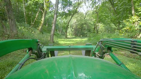 POV-over-the-hood-a-loader-with-forks-driving-down-a-grassy-path-in-the-woods