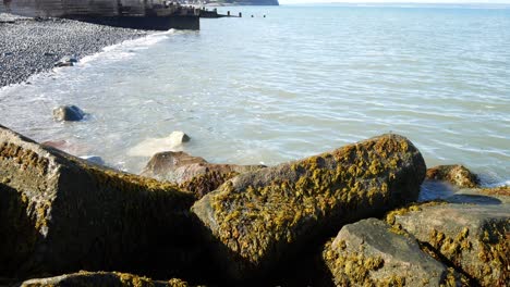 Sunny-blue-ocean-tide-washing-onto-stone-pebble-beach-coastline-tourism-holiday-scene