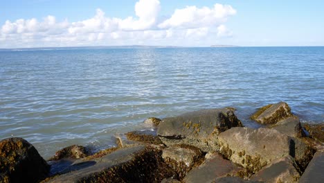 Sunny-blue-ocean-horizon-over-stone-pebble-beach-coastline-clear-holiday-scene