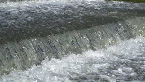 Splashing-water-flows-over-a-small-artificial-cascade-waterfall-closeup-angle-view