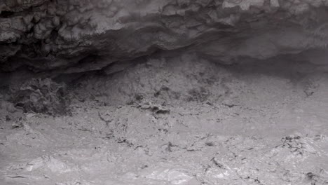 Close-up-of-geothermal-mud-pot-water-exploding-in-slow-motion-under-mud-volcano-overhang