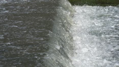 Splashing-water-flows-over-a-small-artificial-cascade-waterfall-closeup-side-view