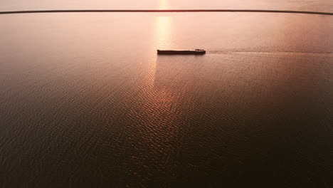 Ship-In-Silhouette-Over-The-Calm-Sea-In-Lelystad,-Flevoland,-Netherlands-On-A-Glorious-Sunset---aerial-drone