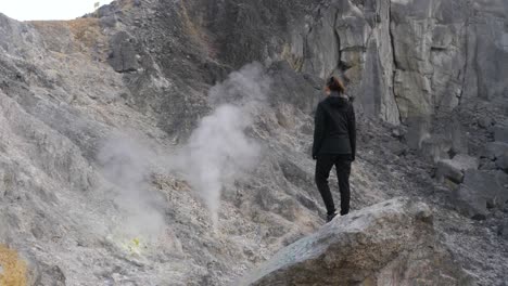 Slow-motion-shot-of-woman-standing-on-rock-looking-at-sulfur-smoke-from-volcano-in-North-Sumatra,-Indonesia