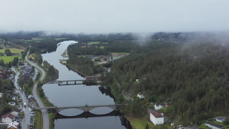 Aerial-drone-view-over-the-Amfoss-bridge-on-the-Nidelva-river,-in-the-Aamli-town,-dark,-foggy-day,-in-South-Norway