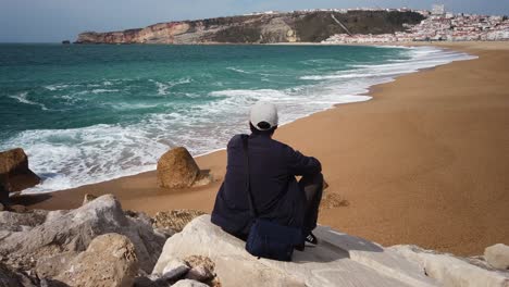 Young-man-sitting-on-a-rock-watching-breaking-waves