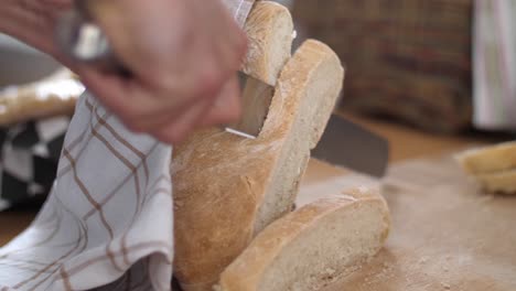 A-slice-of-white-bread-being-cut-from-a-bread-loaf-with-a-knife-on-a-wooden-cutting-board-while-another-slice-of-bread-is-laying-beside