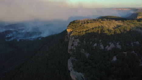 Smoke-rising-from-forest-landscape-during-bushfires,-forward-aerial