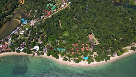 Aerial-down-shot-of-Tropical-Island-small-bungalow-resorts,-drone,-bird’s-eye-view-down-shot-with-lush-green-rain-forest-and-tropical-palm-trees-with-white-sand-beach
