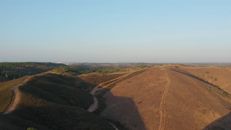 Aerial-forward-shot-of-beautiful-barren-and-dry-hills-and-dirt-trails-with-Portimão-city-into-the-distance-in-Algarve,-Portugal