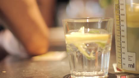 Close-up-of-a-a-glass-of-lemonade-with-a-lemon-slice-in-it-and-a-person-sitting-in-the-blurred-background