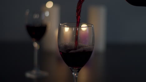 Rotwein-Wird-In-Glas-Mit-Einem-Vollen-Glas-Und-Brennenden-Kerzen-Im-Hintergrund-Gegossen