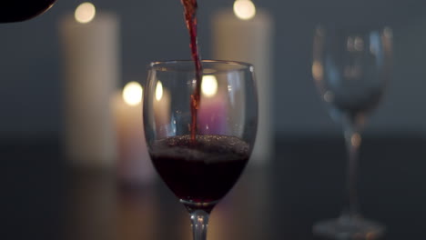 Rotwein-Wird-In-Glas-Mit-Kerzen-Im-Hintergrund-Gegossen