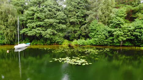 Bosque-Junto-Al-Lago-De-Agua-Verde-Cristalino-Con-Un-Bote-Flotando-De-Costado-En-Pradzonka,-Norte-De-Polonia