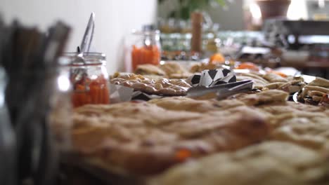 Close-up-of-a-mediterranean-buffet-with-pita-and-focaccia-bread-laying-in-the-foreground-and-cutlery-beside-with-carrot-sticks-and-more-food-in-the-background