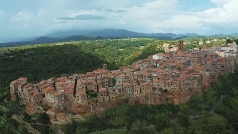 Drone-footage-of-the-ancient-medieval-town-Pitigliano,-a-landmark-of-historic-architecture-on-a-natural-rock-in-the-idyllic-landscape-of-Tuscany,-Italy-with-green-trees-and-storm-clouds
