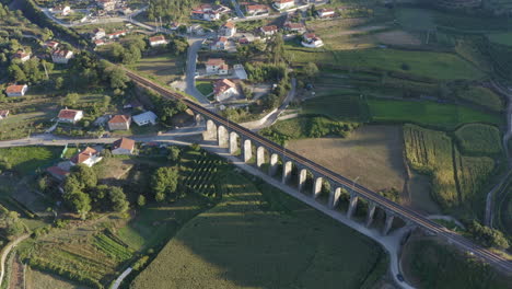 Aerial-shot-circling-around-Old-arch-railway-bridge-surrounded-by-crop-fields,-casting-shadow-on-corn-field---Ponte-Seca,-Durrães,-Barcelos