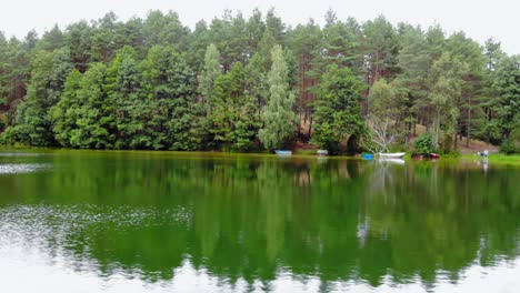 Drone-Flying-Over-The-Verdant-Water-Of-Calm-Lake-Overlooking-The-Lush-Green-Coniferous-Forest-In-Pradzonka,-Poland