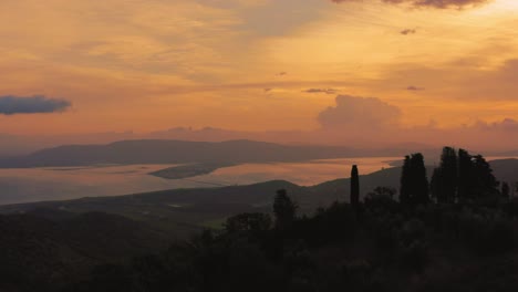 Aerial-footage-of-the-iconic-Monte-Argentario-bay-lagoon,-facing-the-ancient-old-town-Orbetello-close-to-the-Maremma-nature-park-in-Tuscany,-Italy-with-dramatic-clouds-covering-the-sky-at-sunrise