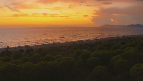 Aerial-drone-footage-of-the-sunset-at-a-sandy-beach-at-the-seaside-in-the-iconic-Maremma-nature-park-in-Tuscany,-Italy,-with-a-dramatic-thunderstorm-cloud-sky-and-wooden-tipis-along-the-empty-beach