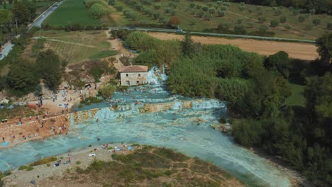 Aerial-drone-footage-of-the-famous-Saturnia-Cascate-del-Mulino-thermal-hot-springs-with-its-blue-warm-water-near-Grosseto-in-the-idyllic-landscape-of-Tuscany,-Italy-with-hills-and-olive-trees-around