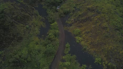 Drone-aerial-of-cars-driving-off-road-on-a-forest,-revealing-landscape-and-mountains,-during-a-camping-trip-towards-Pacaya-volcano,-Guatemala